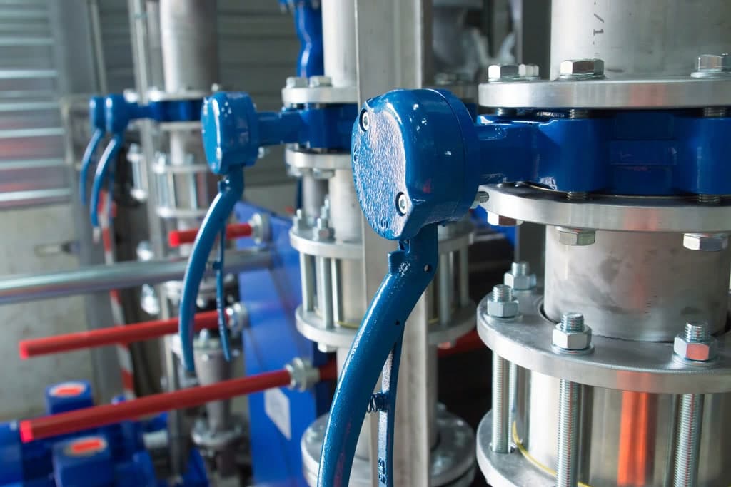 Close-up of a piping system: stainless-steel pipes with flanges and blue butterfly valves with hand levers.
