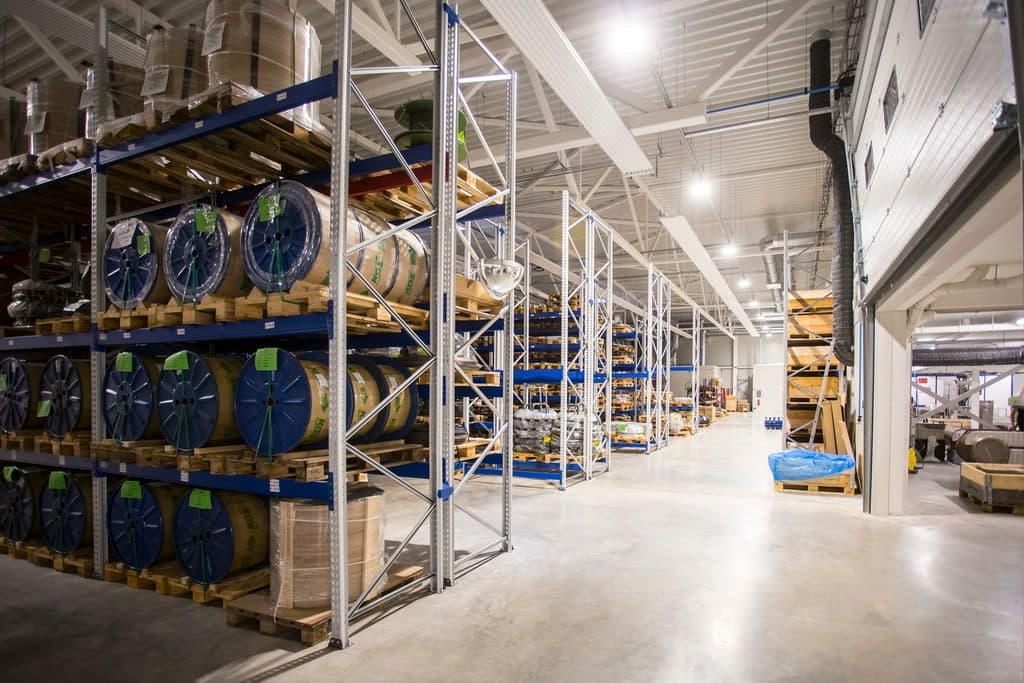 Helles Lager mit Palettenregalen, in denen Kabeltrommeln und Kartons liegen, dahinter weitere Regalreihen.
